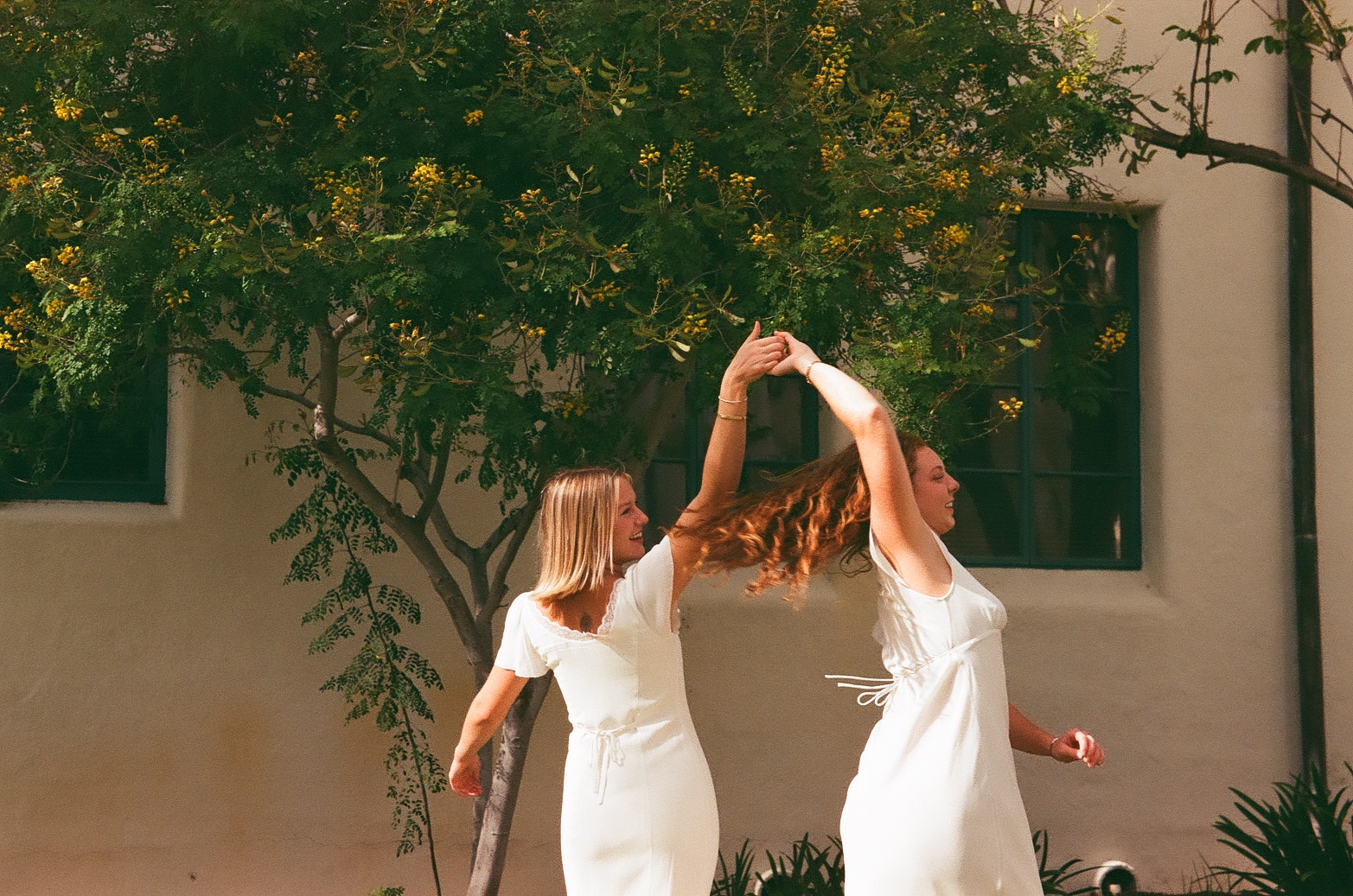 Annabelle and Kiera dancing together in white dresses under a yellow flowering tree