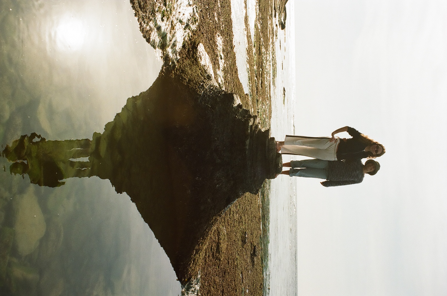 Kiera and Kayden standing on a rock with their reflection in the tide pool below
