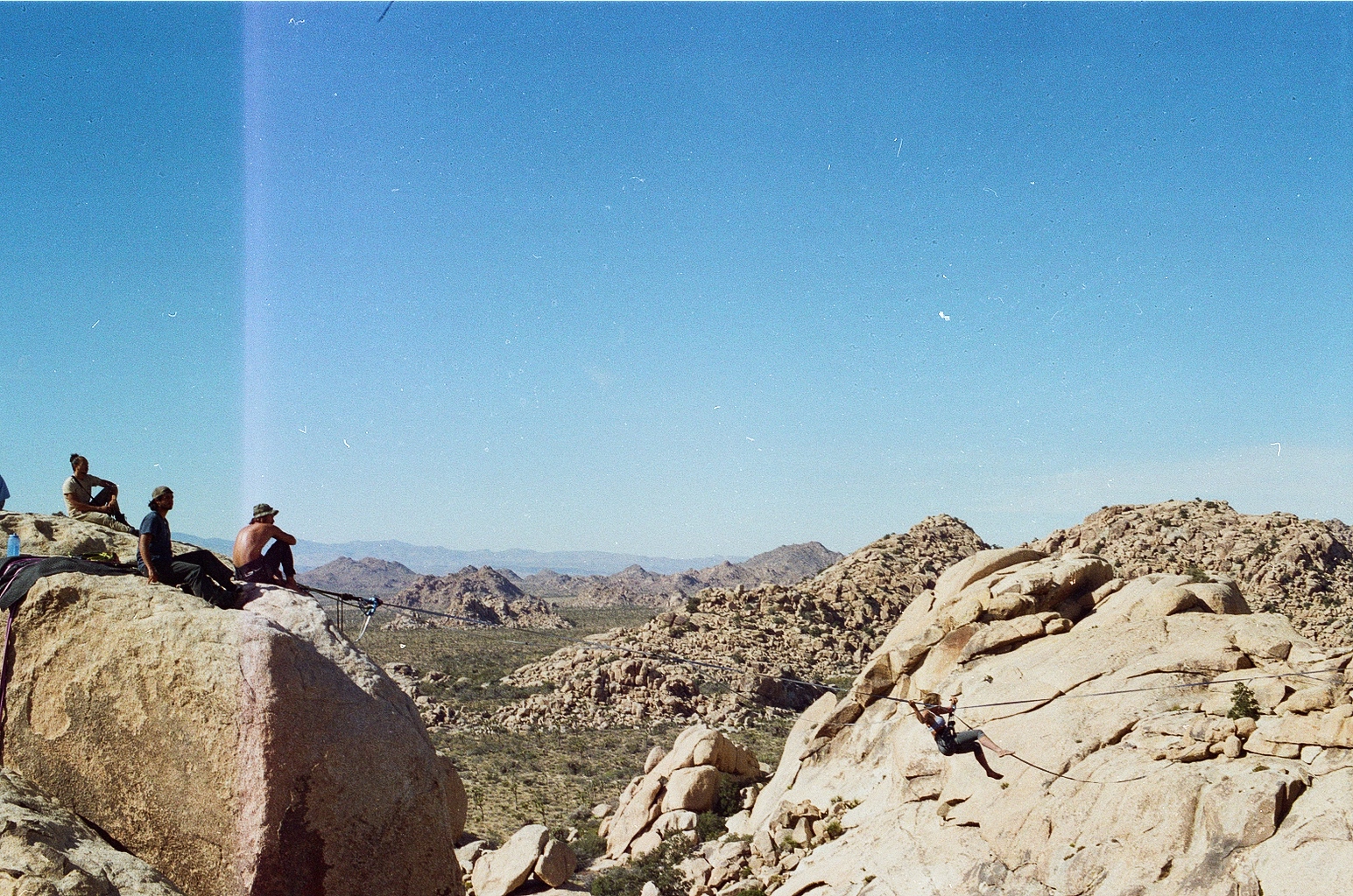 Rock climbers on granite boulders above a sweeping Joshua Tree valley
