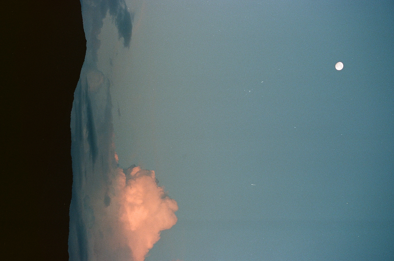 Moon rising above a silhouetted ridge with a glowing pink cloud