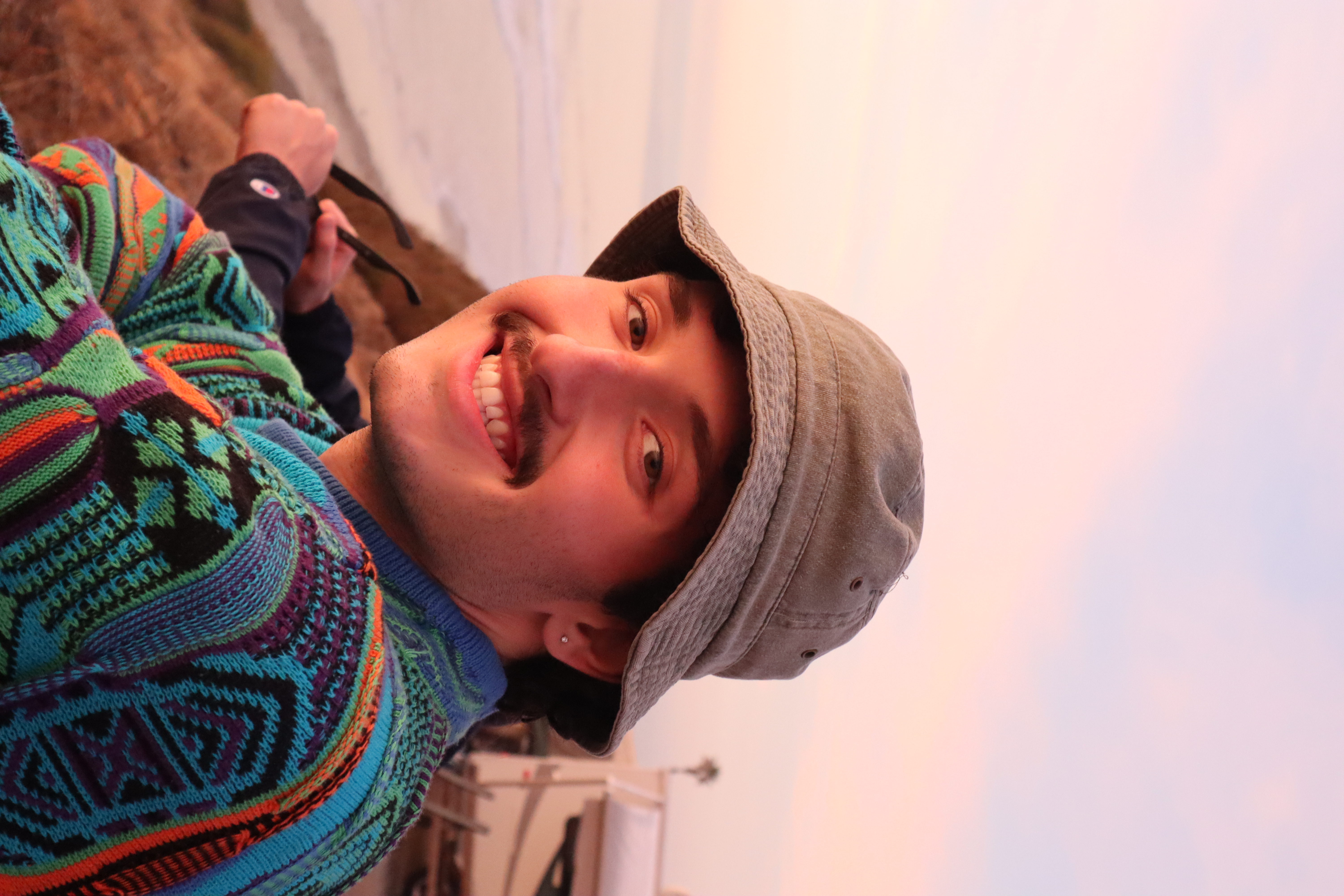 Nick smiling at sunset wearing a bucket hat and colourful sweater
