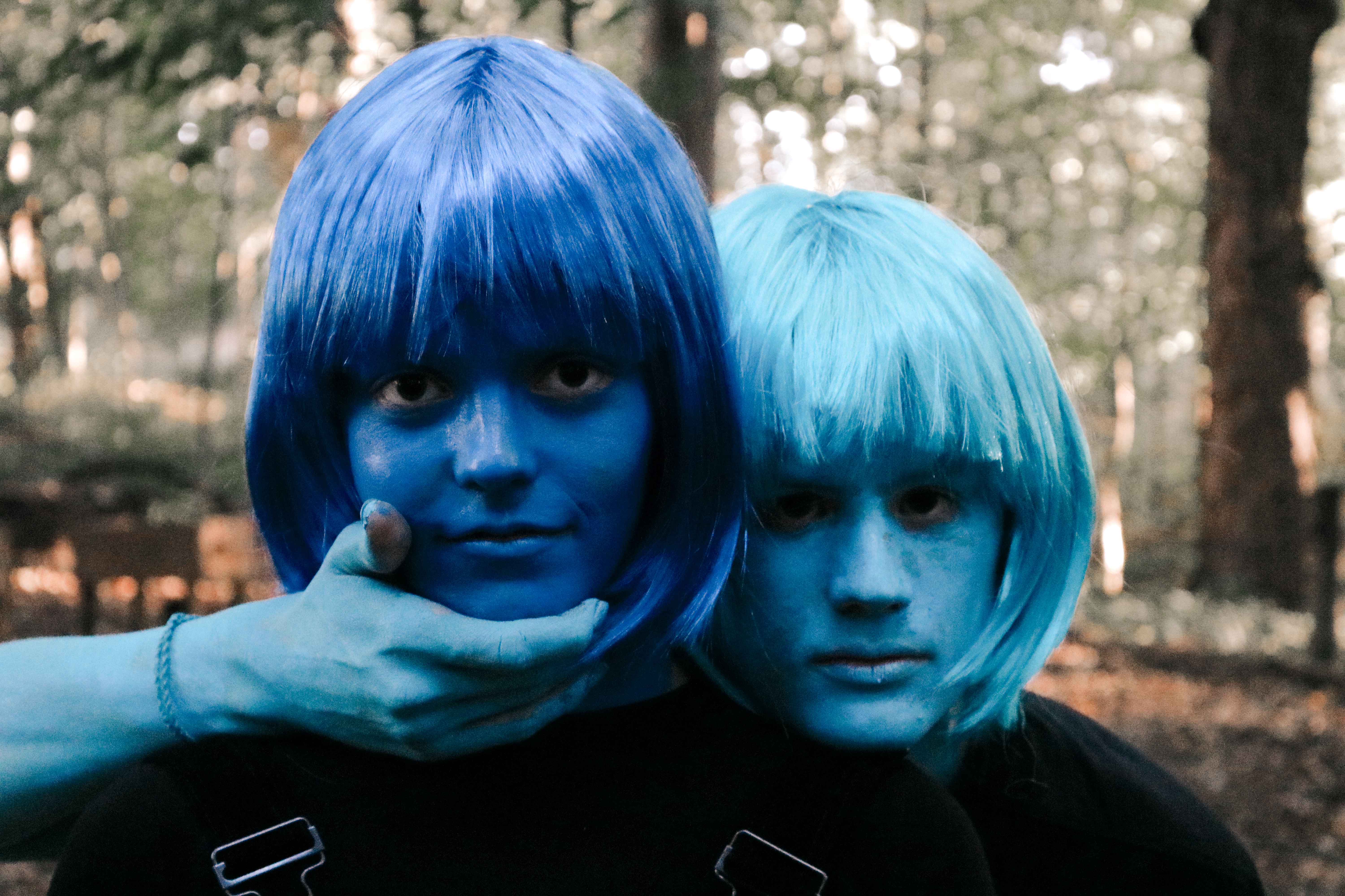 Two figures with blue body paint and wigs close together in the forest