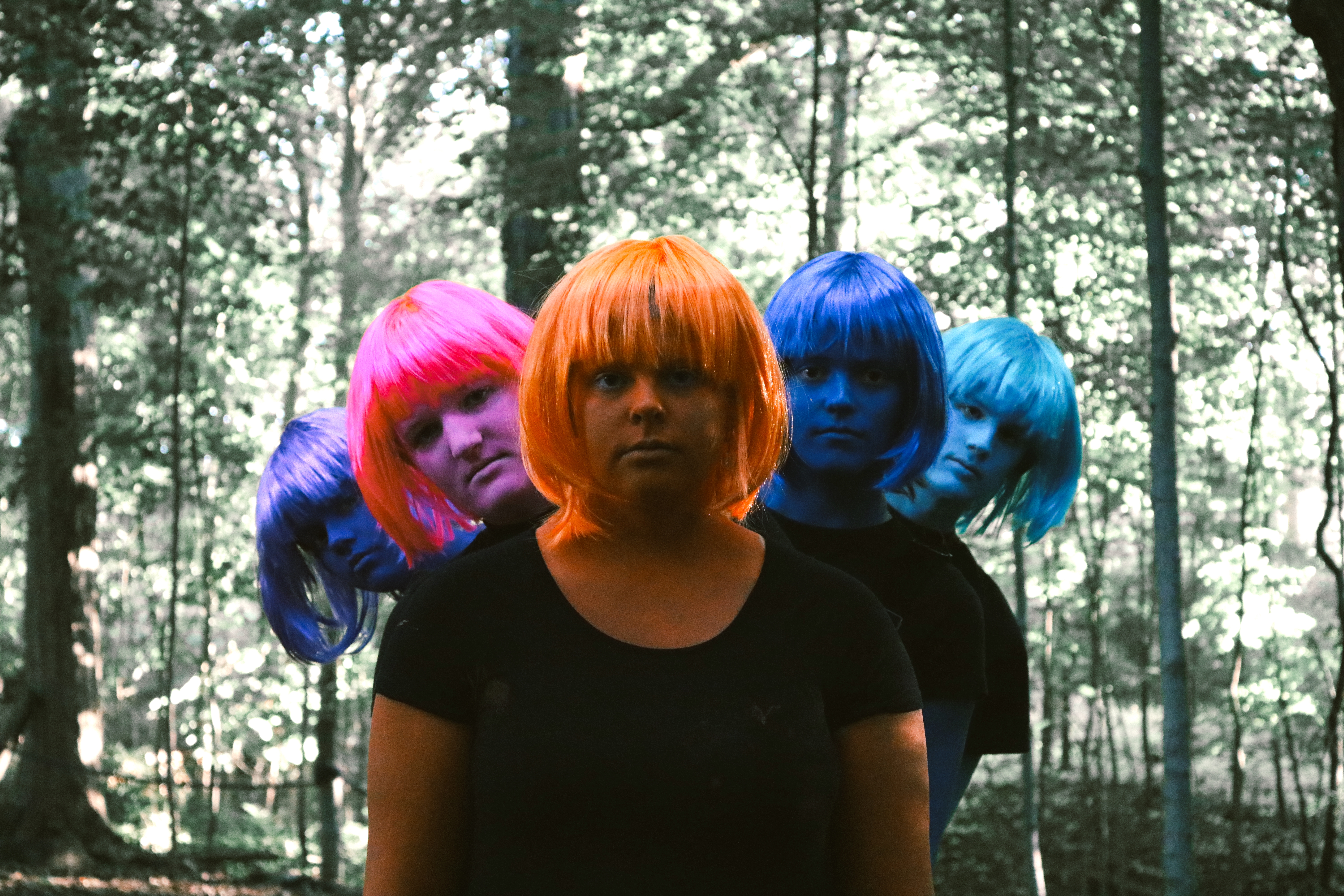 Four figures with color body paint and wigs standing in a forest