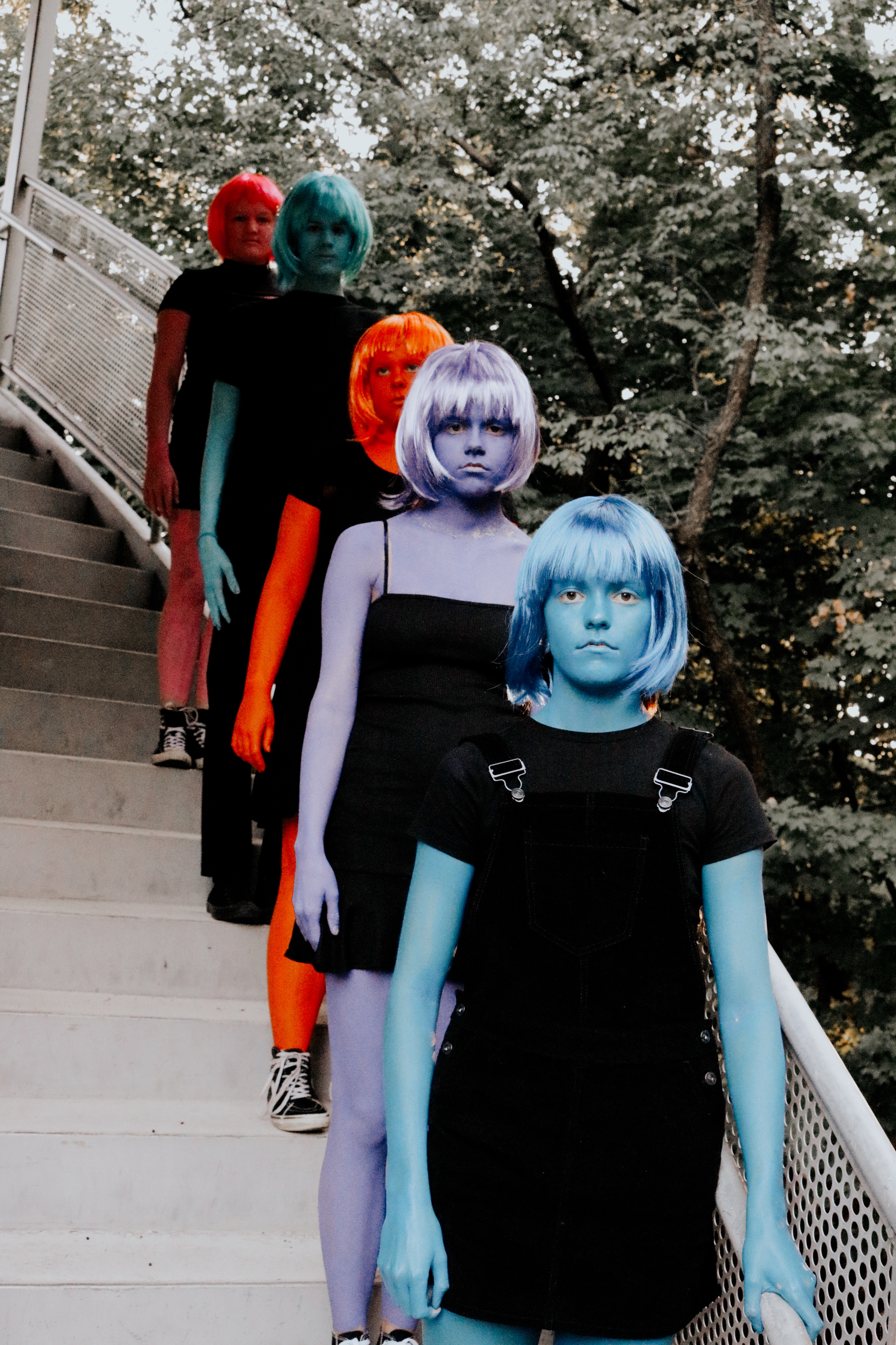 Four figures with full-body color paint and colored wigs descending outdoor stairs