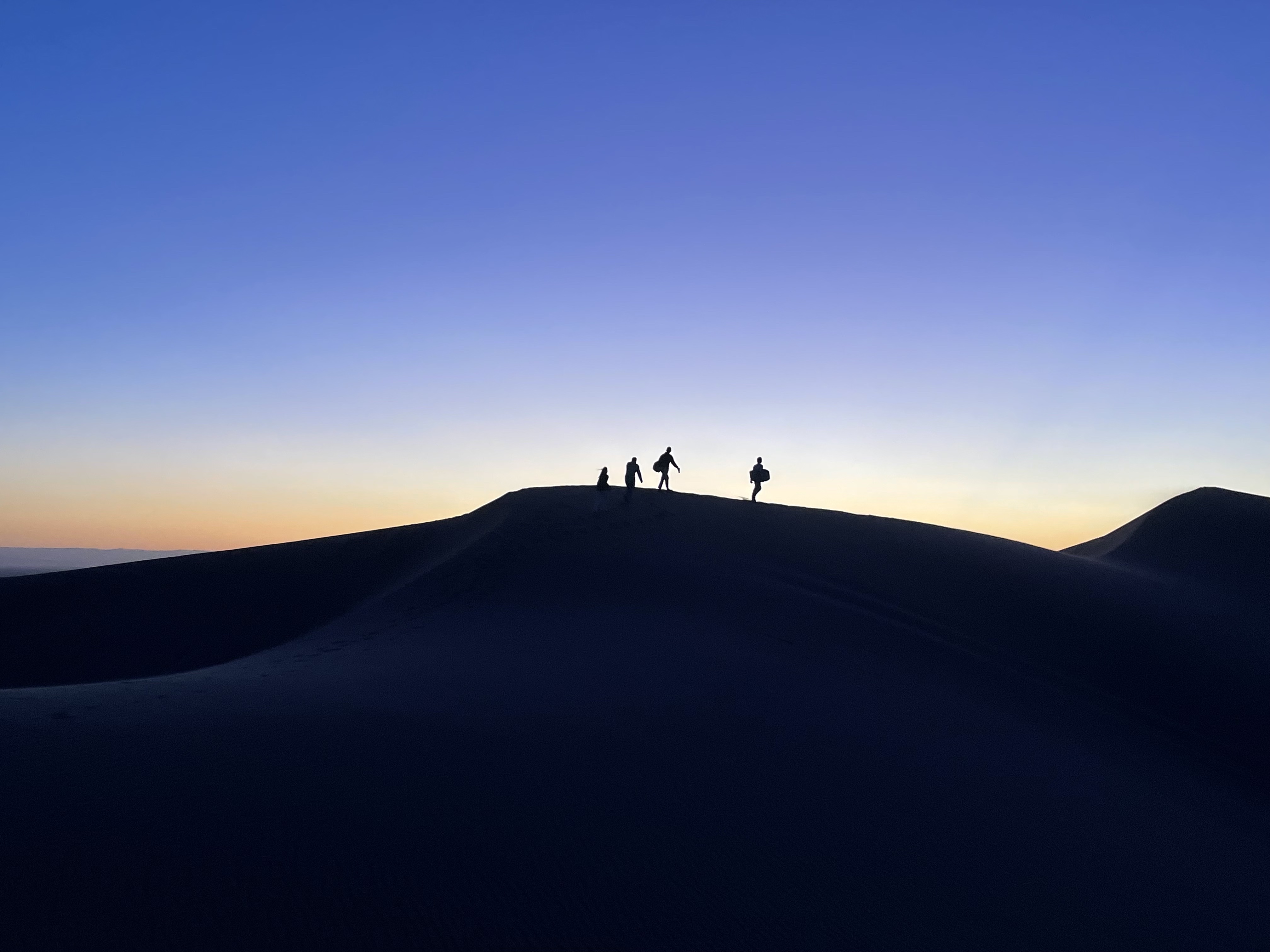Silhouettes of people walking on desert dunes at sunset
