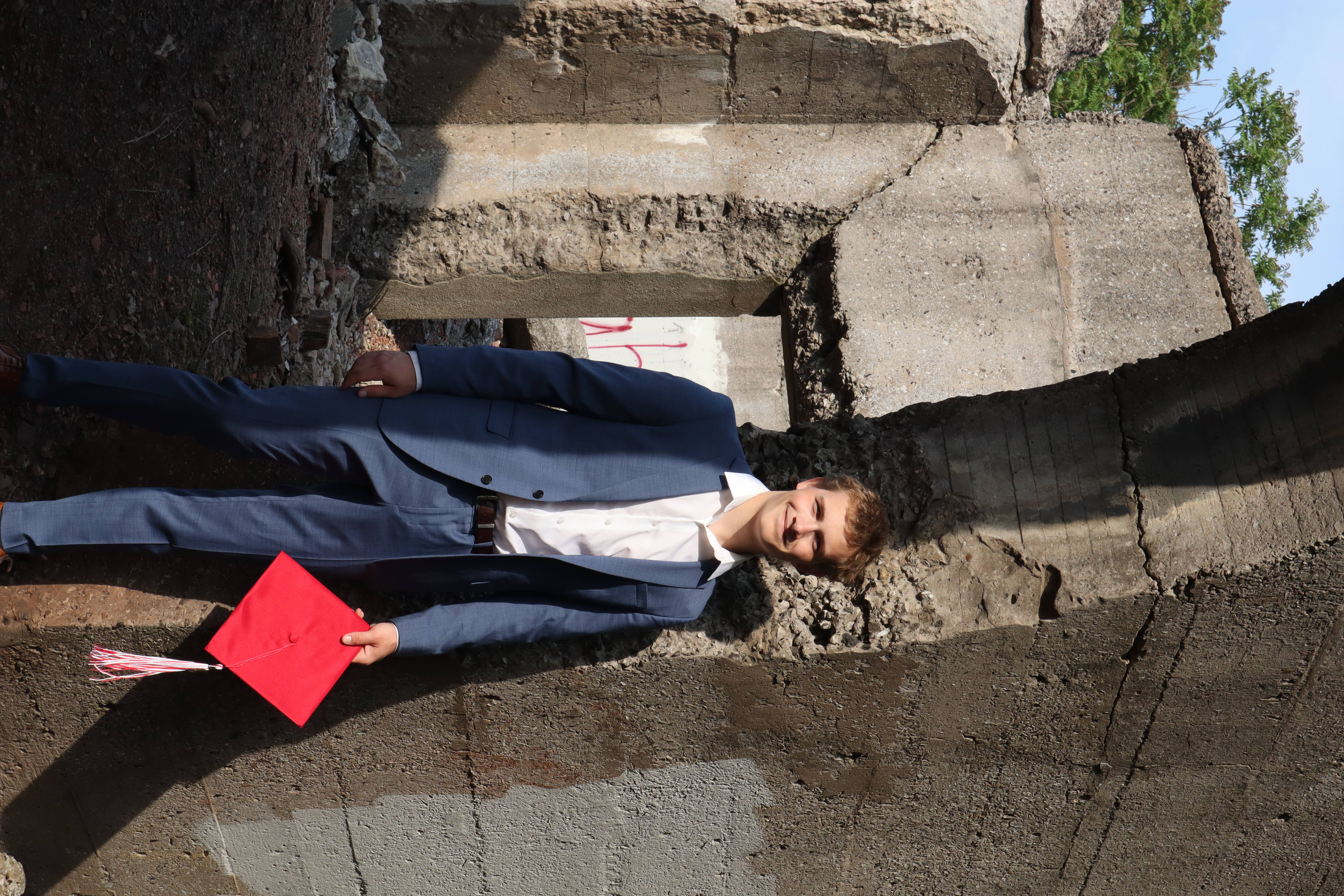 Mason in blue suit holding his red graduation cap among concrete ruins