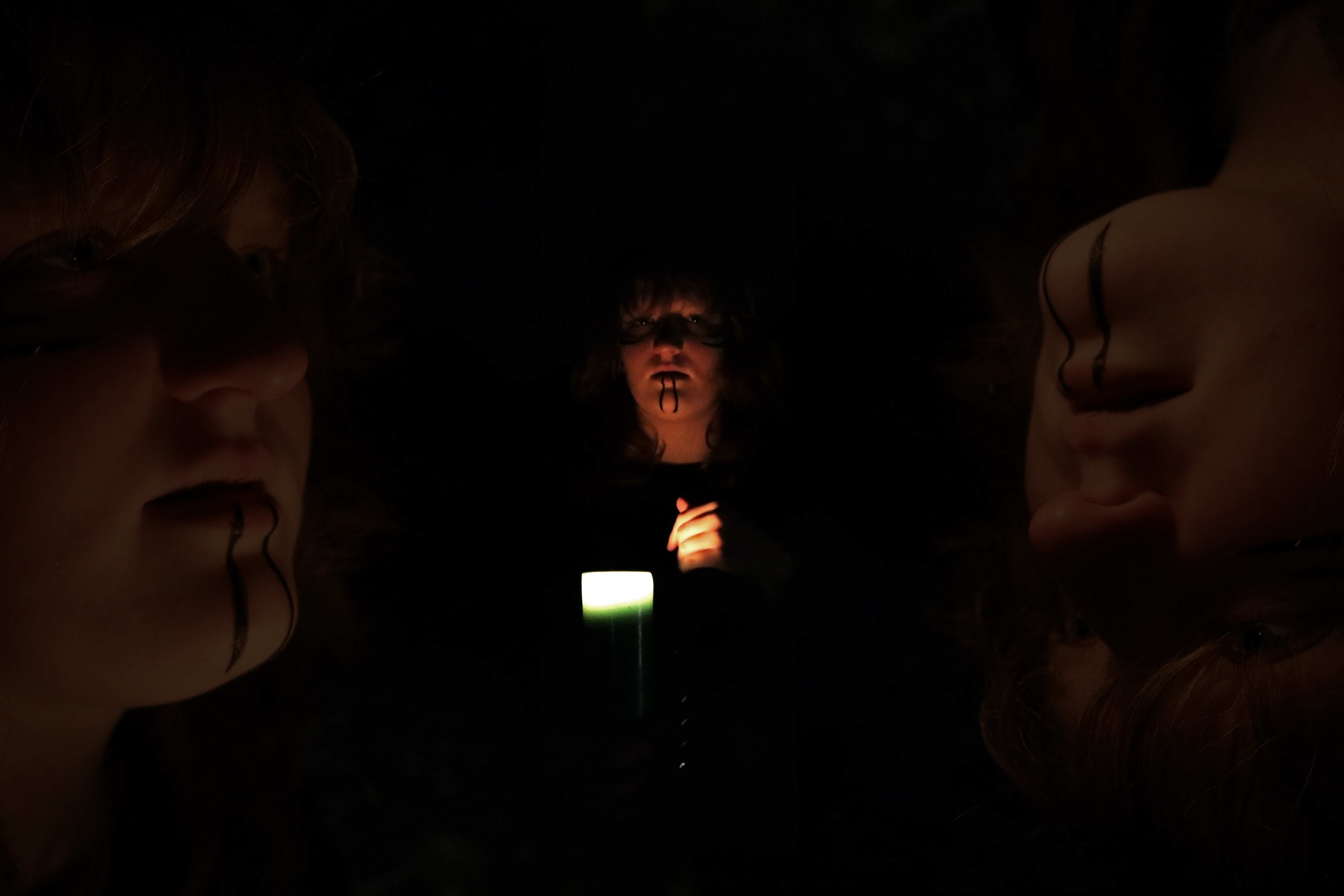 Three figures in darkness lit by a single candle with dramatic face paint