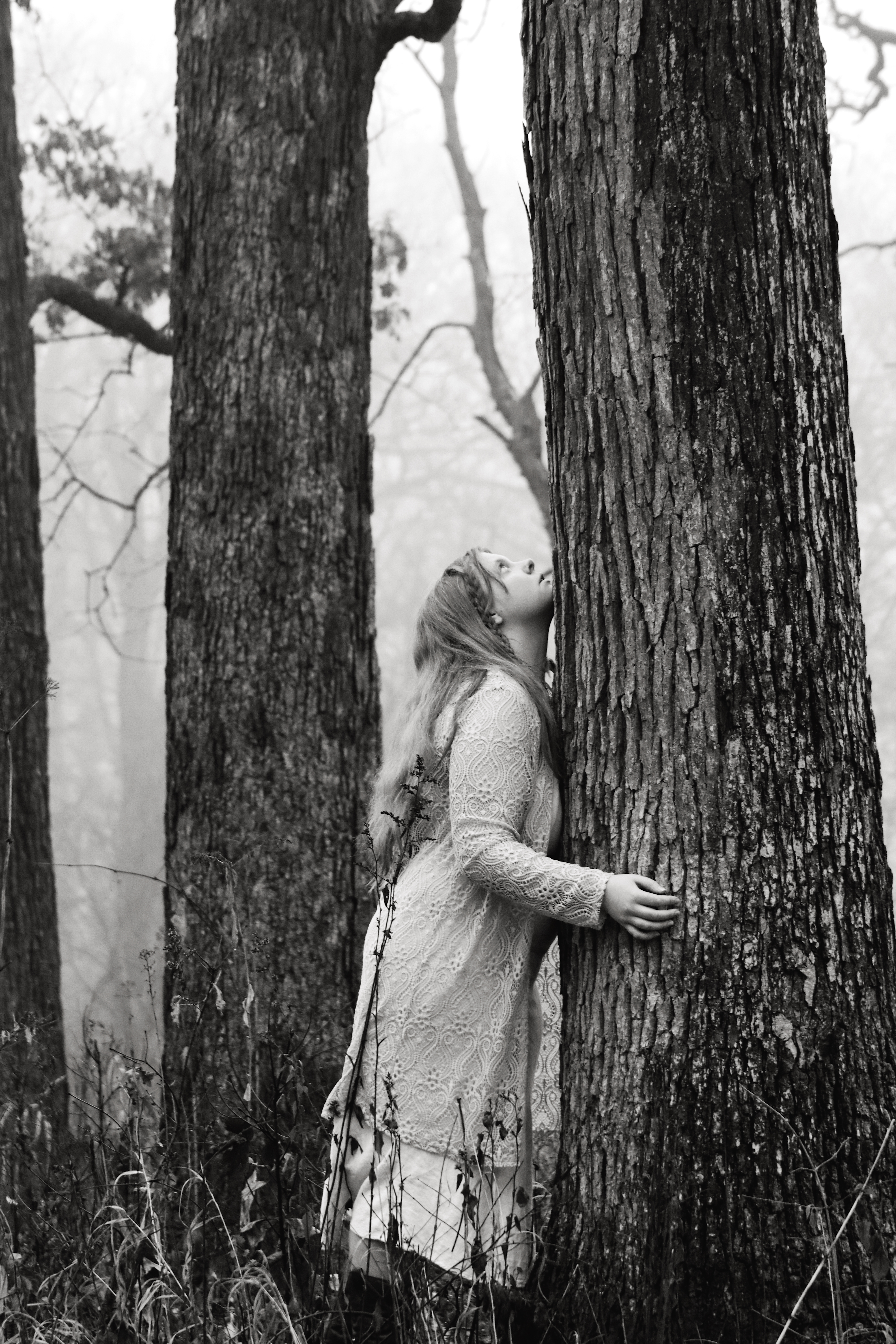 Woman in lace dress leaning against a tree in a foggy forest, black and white