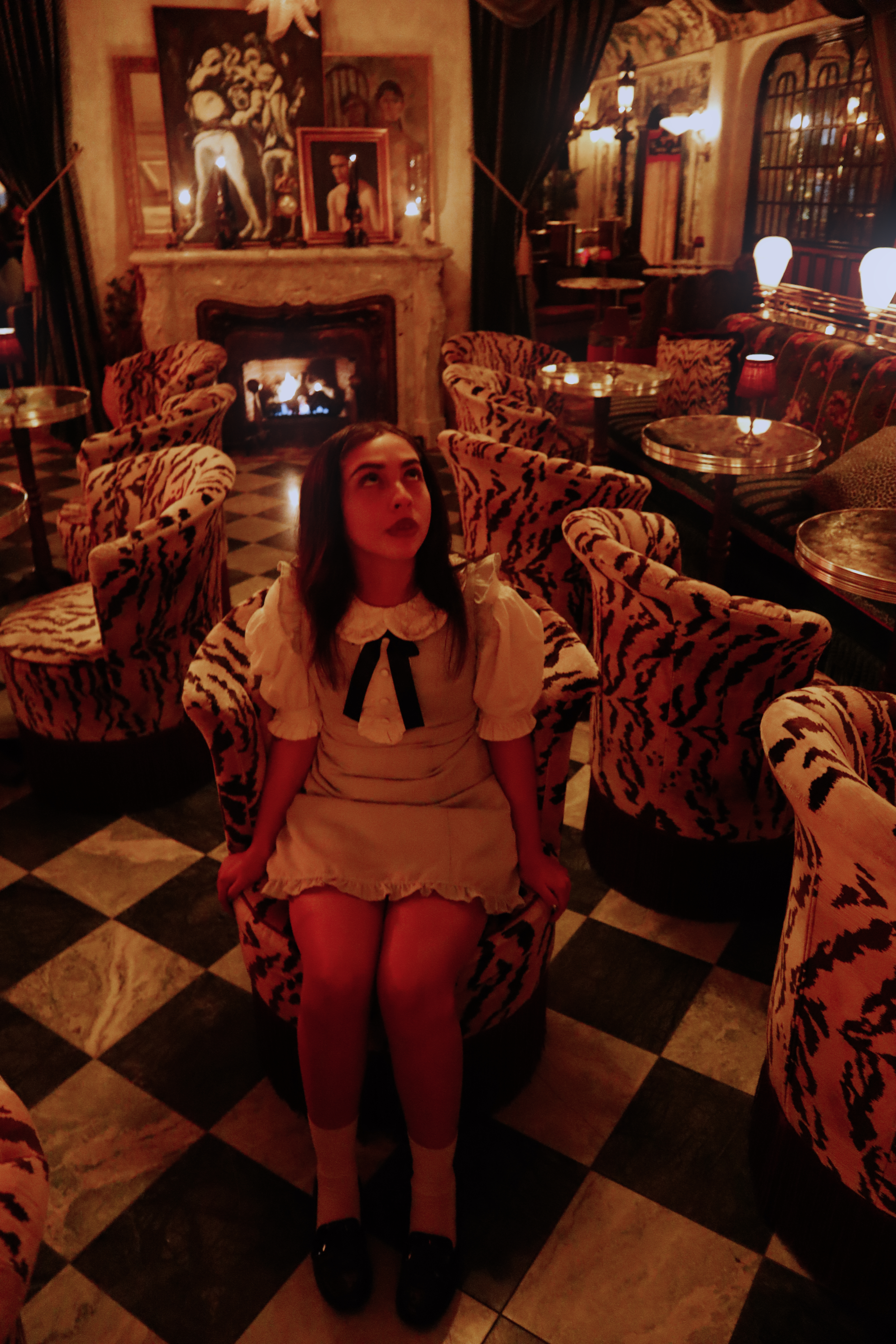 Woman in white dress seated in tiger print chair looking up, fireplace behind her