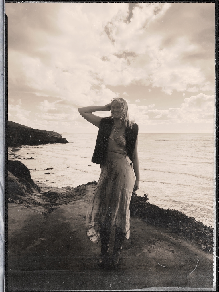 Sophia standing on coastal cliffs by the ocean, sepia toned film photo