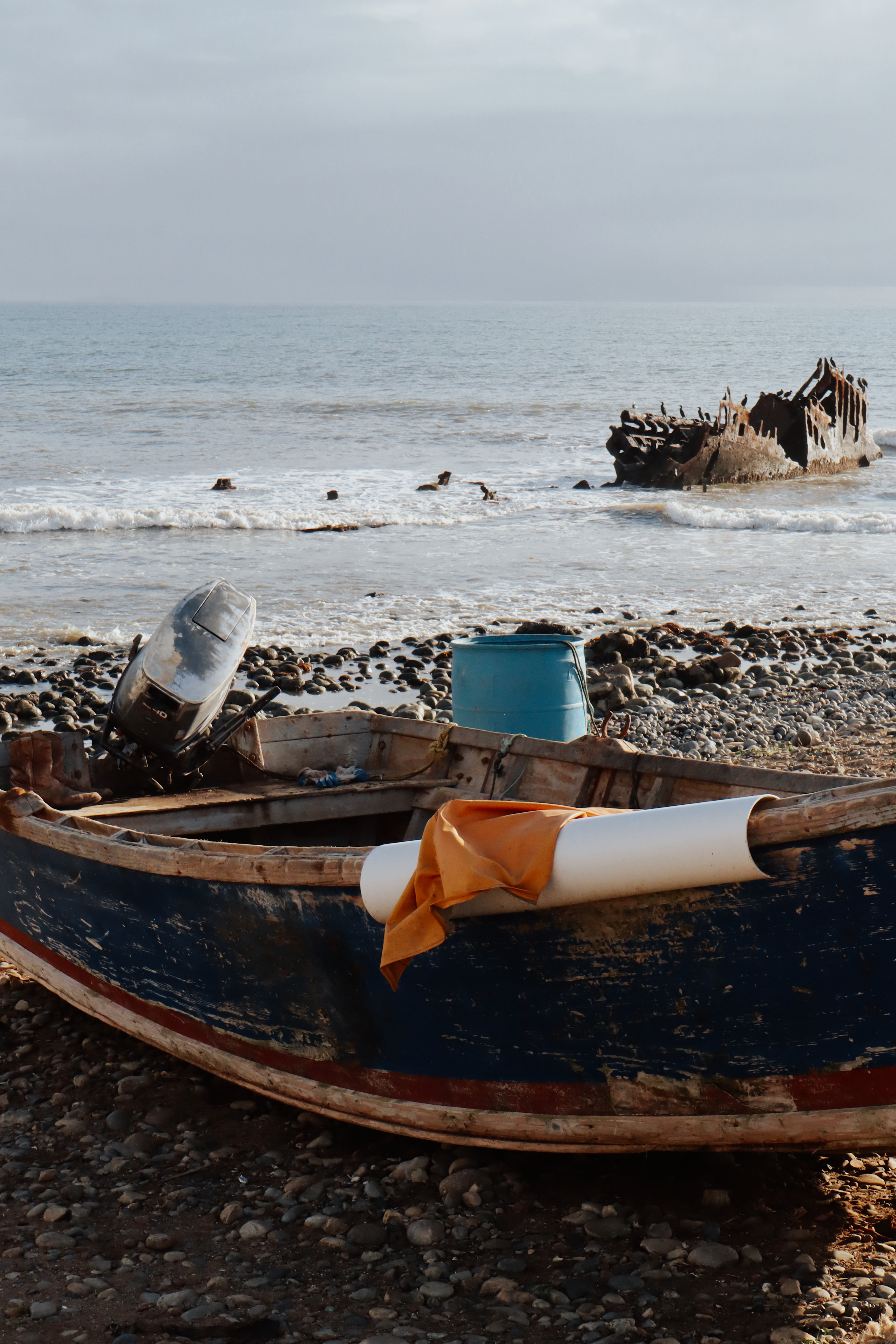 Old fishing boat on a rocky beach with a shipwreck in the surf behind