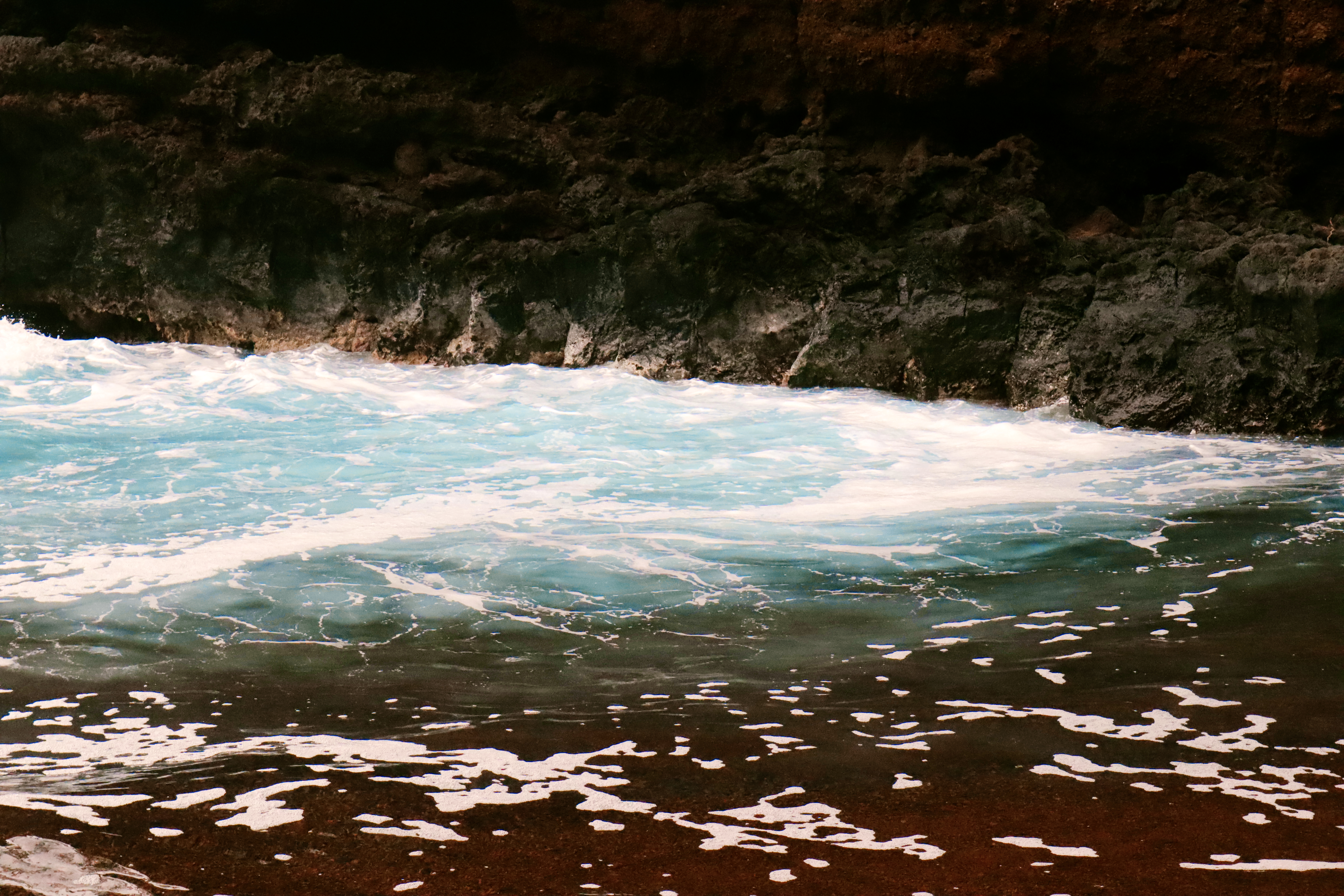 Turquoise waves crashing against dark volcanic rock on a black sand beach