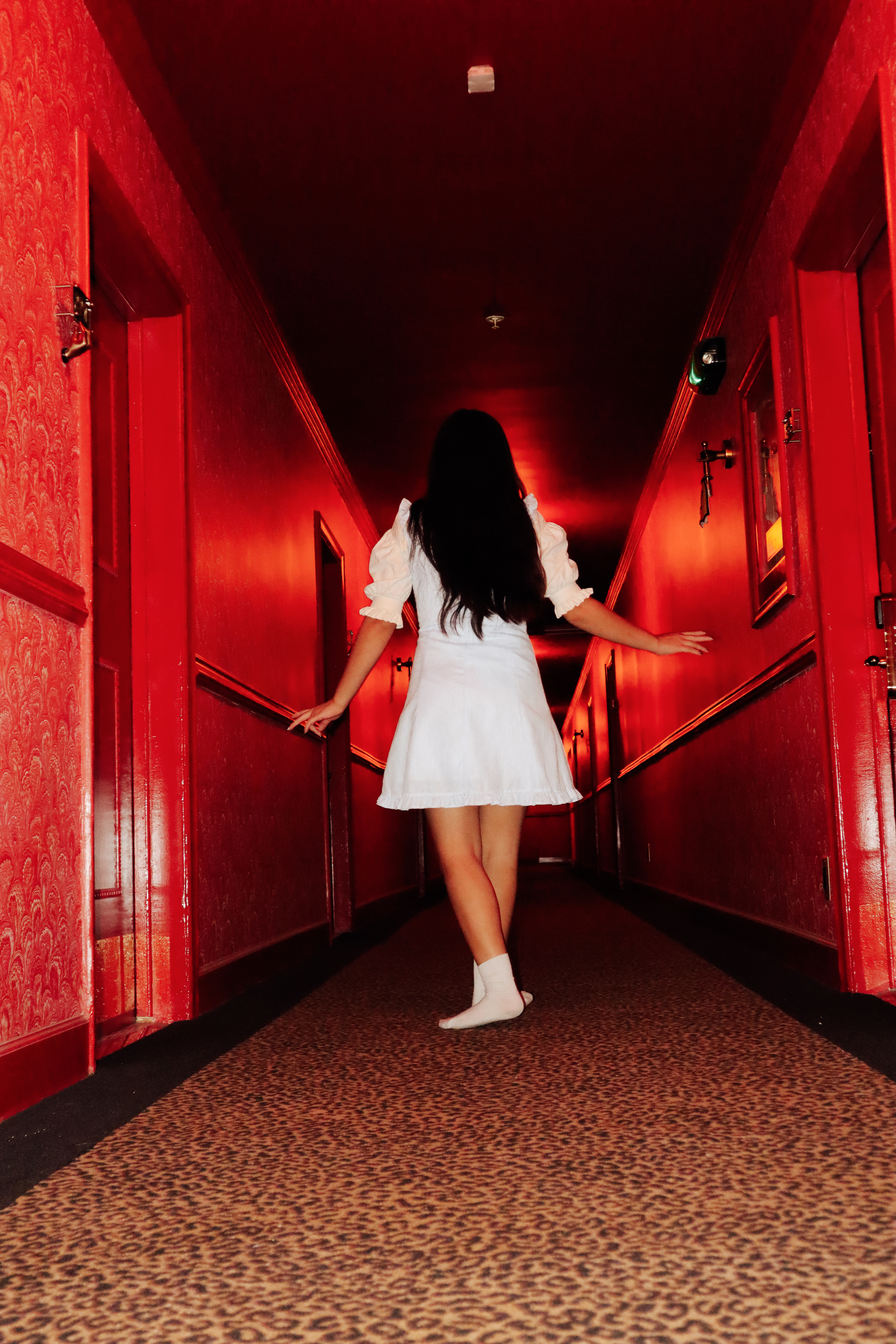 Woman in white dress walking away down a red corridor with arms outstretched