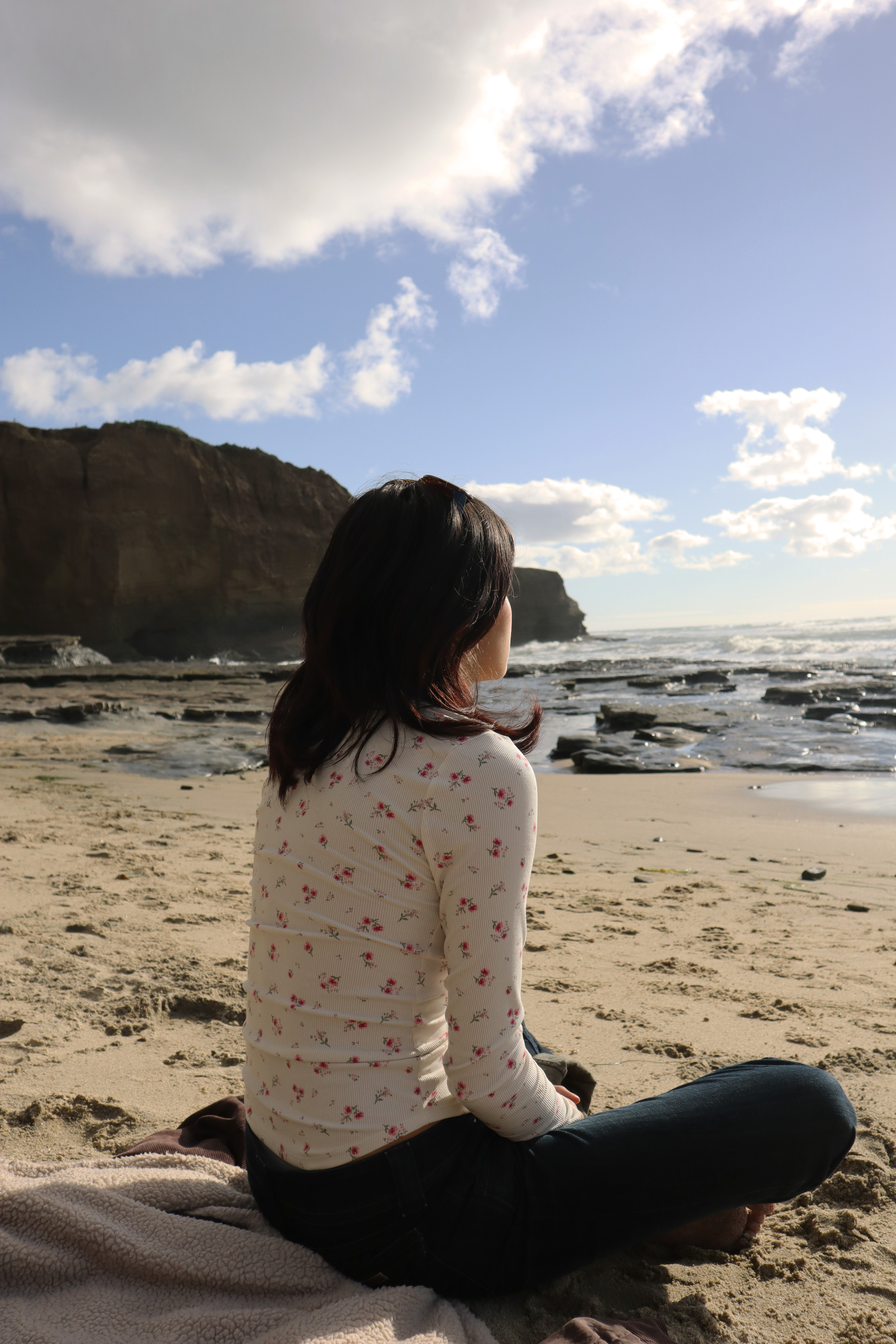 Edana sitting cross legged on the beach looking out to sea