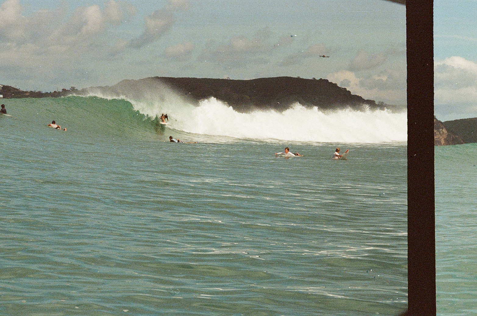 Surfers paddling as a big green wave breaks behind them