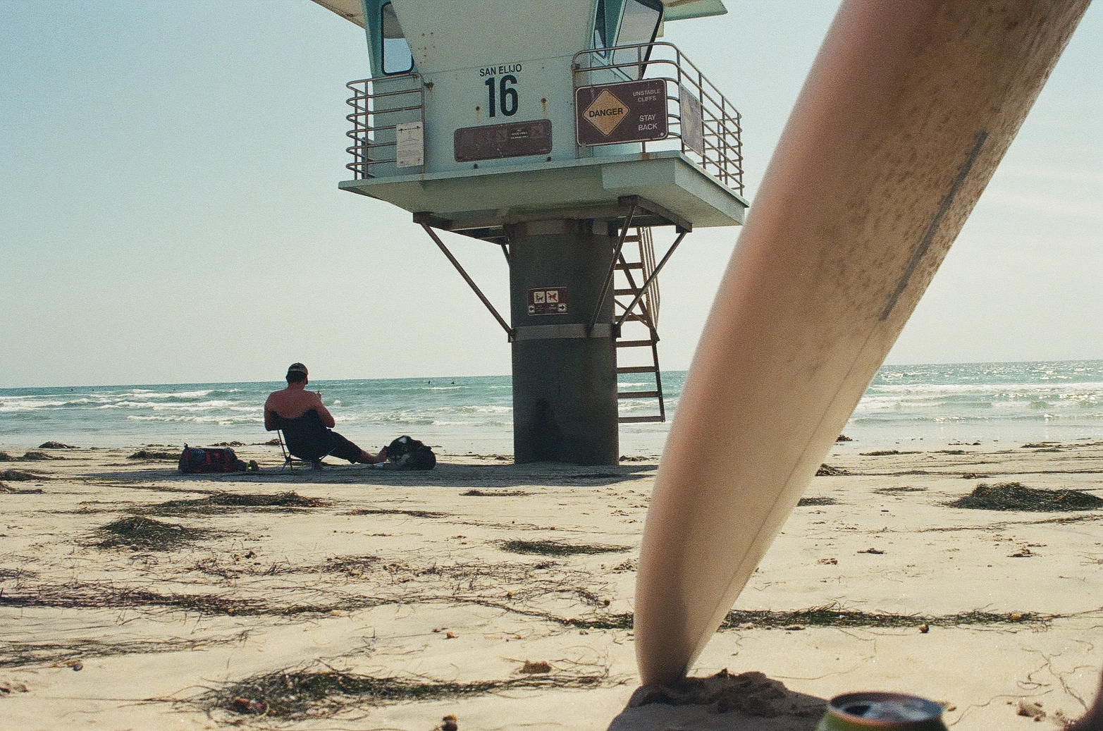Surfboard nose in foreground with a surfer resting under San Elijo lifeguard tower 16, California