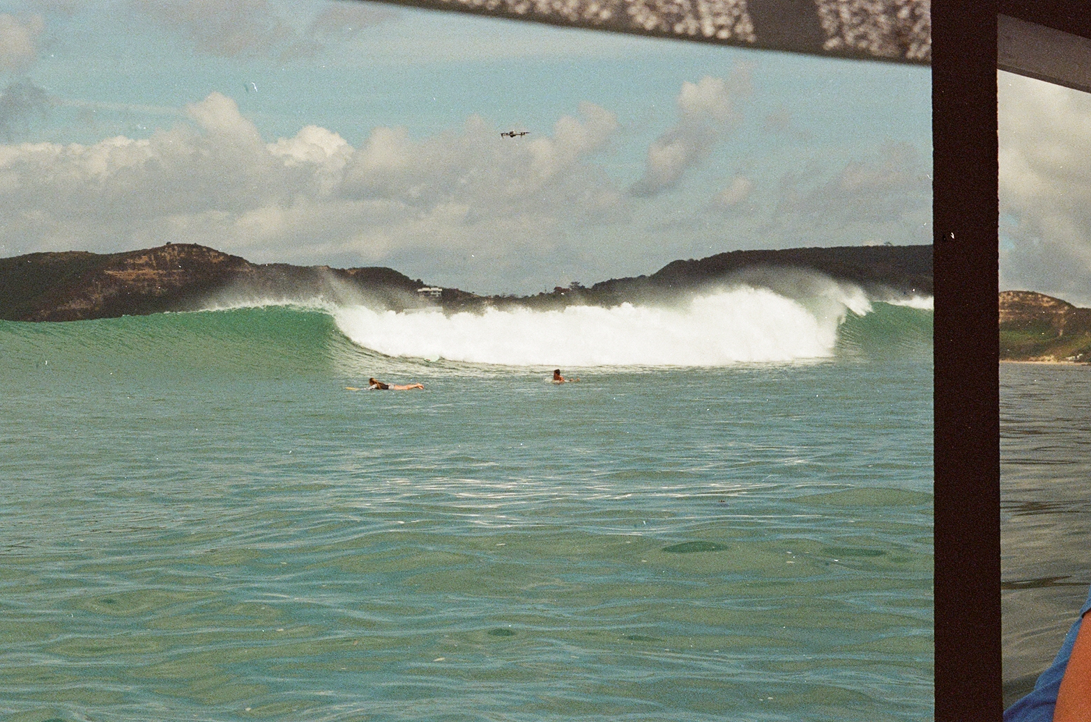 Two surfers paddling toward a massive crashing wave