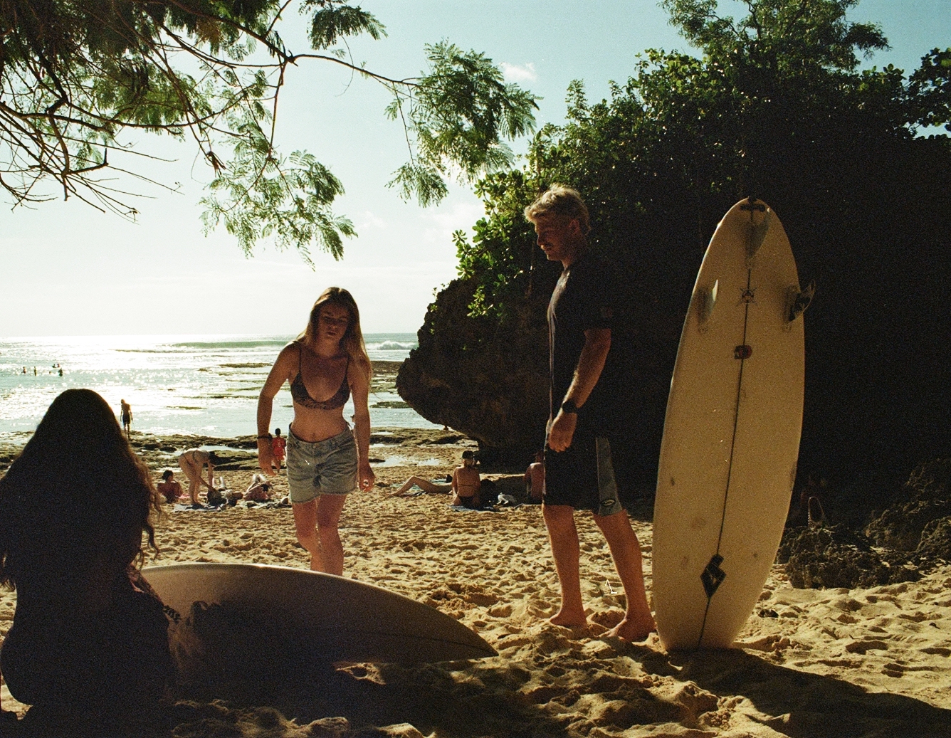 Surfers on a tropical beach in warm golden light beneath lush jungle cliffs